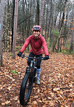 Smiling Woman riding mountain bike in leaf-covered forest.